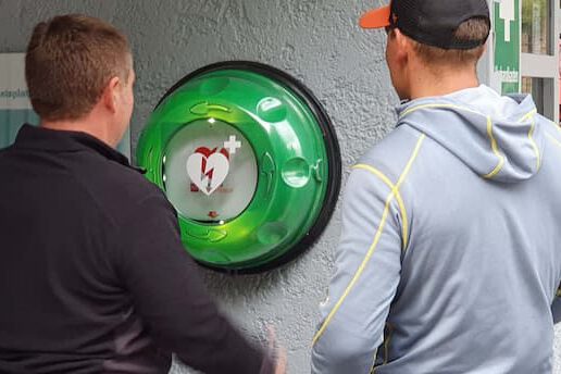 Defibrillator am Eisplatz Zwei Personen stehen vor einem Defibrillator an der Wand des Eisplatzes Lindenberg.