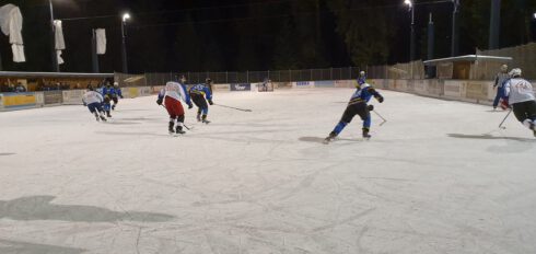 Eishockeyspiel auf beleuchtetem Außeneisplatz in Lindenberg, Spieler in blauer und weißer Ausrüstung in Aktion.