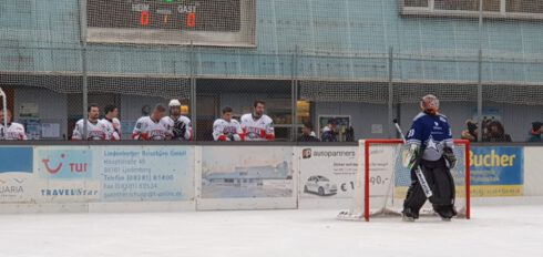 Eishockeyspieler auf der Bank und ein Torwart auf dem Eis, Punktestand 0:0, Werbung im Hintergrund.