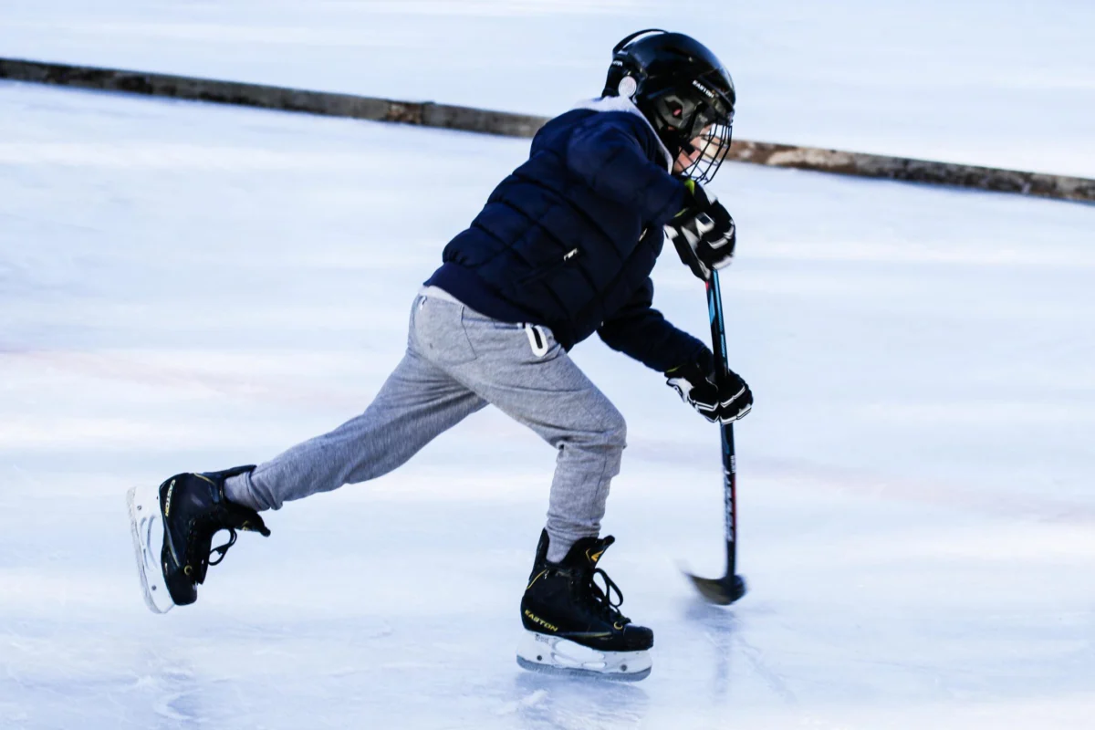 Pondquali_Lindenberg-137 Ein Kind in Eishockeykleidung schießt dynamisch einen Puck über das Eis eines Freiluftstadions.