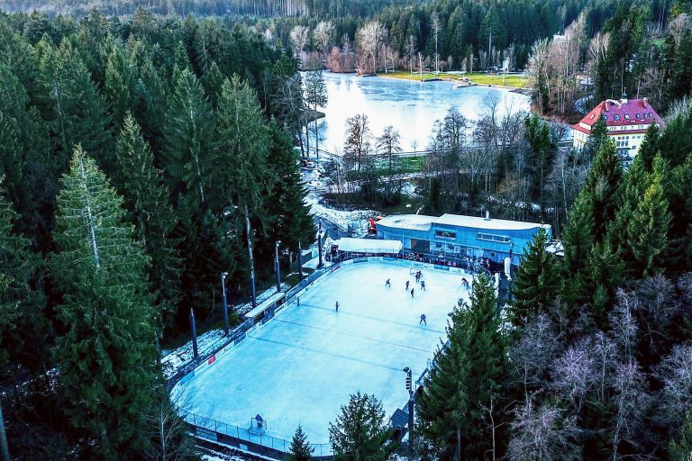 Eisplatz Lindenberg aus der Vogelperspektive, umgeben von dichtem Wald und einem halb zugefrorenen See im Hintergrund.