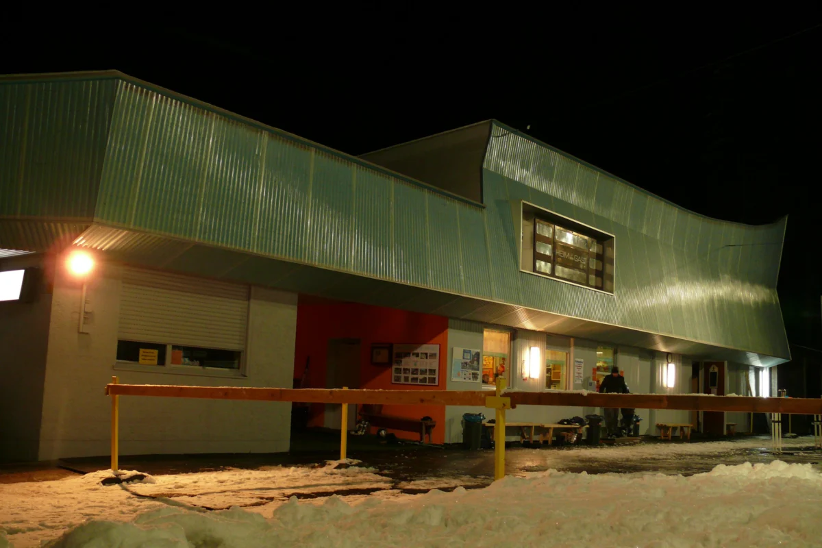 eisstueble lindenberg Das Bild zeigt das beleuchtete Eisstüble am Eisplatz Lindenberg bei Nacht, mit schneebedecktem Vorplatz.