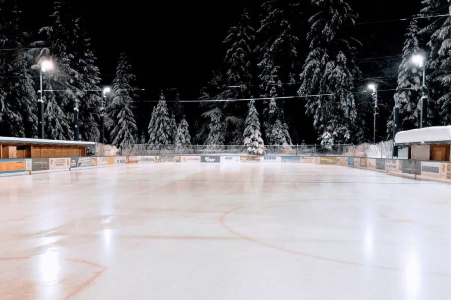 eisplatz-lindenberg-verschneit Verschneiter Eisplatz in Lindenberg, umgeben von beleuchteten Bäumen und Holzhütten in winterlicher Nachtstimmung.
