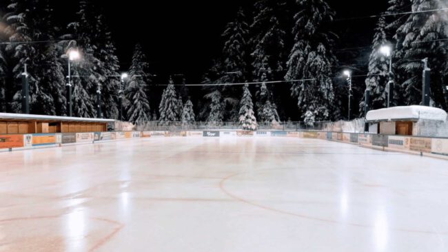 eisplatz-lindenberg-verschneit Verschneiter Eisplatz in Lindenberg, umgeben von beleuchteten Bäumen und Holzhütten in winterlicher Nachtstimmung.