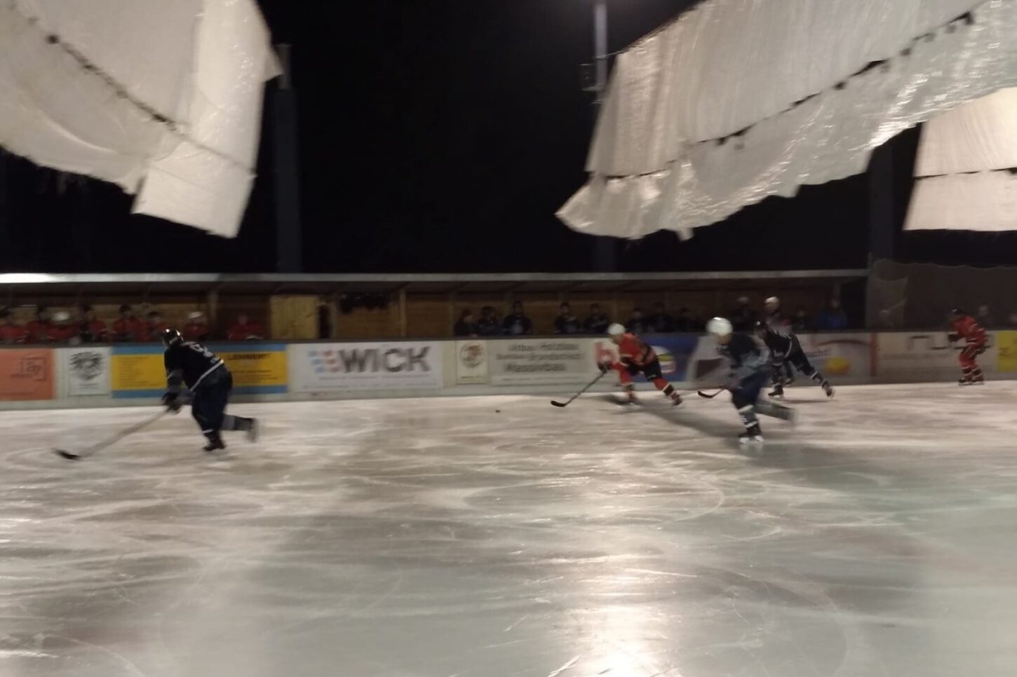 IMG-20211114-WA0015 Mehrere Eishockeyspieler beim nächtlichen Spiel auf dem Eisplatz Lindenberg, umgeben von Zuschauern.
