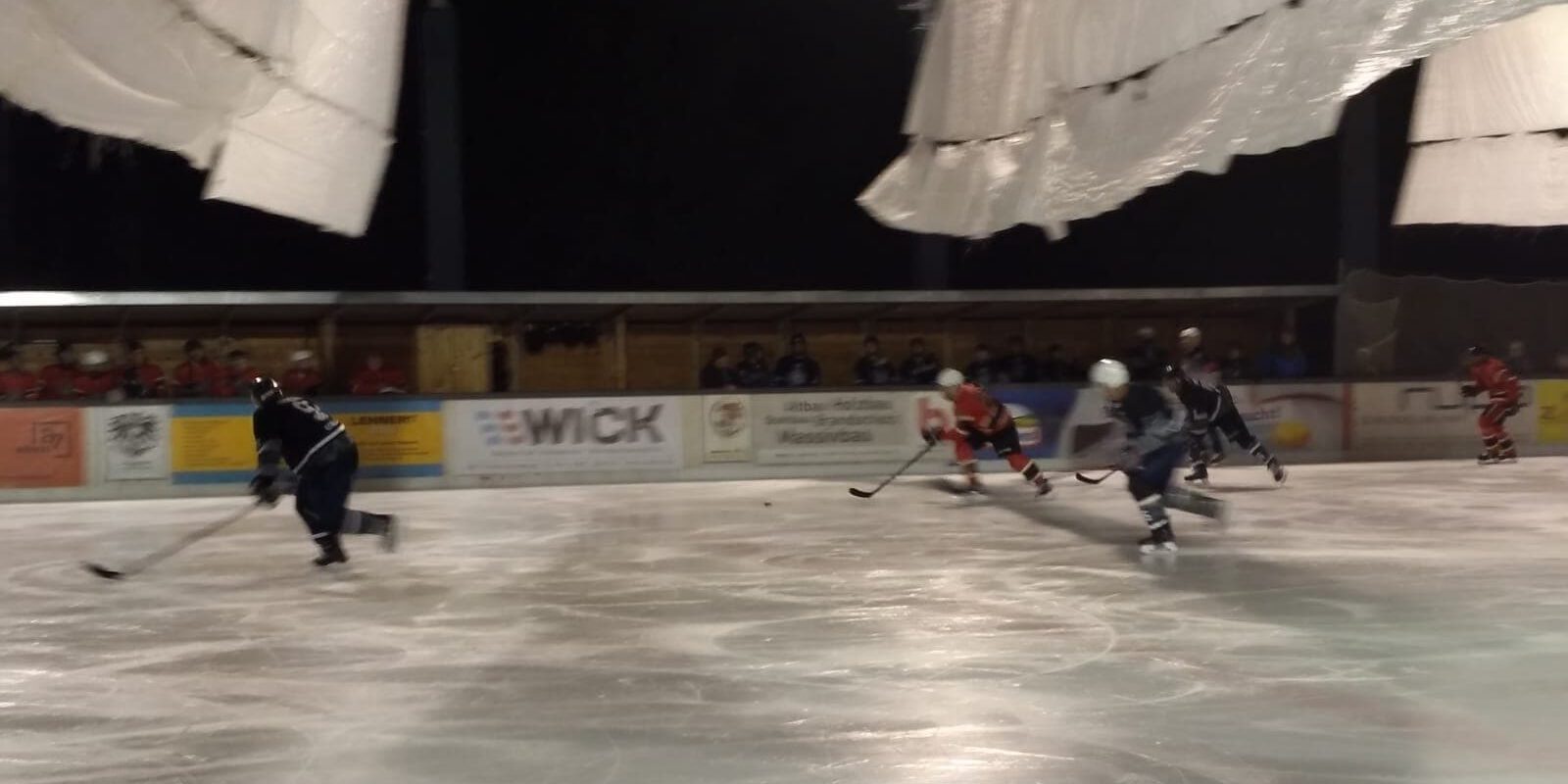 Mehrere Eishockeyspieler beim nächtlichen Spiel auf dem Eisplatz Lindenberg, umgeben von Zuschauern.