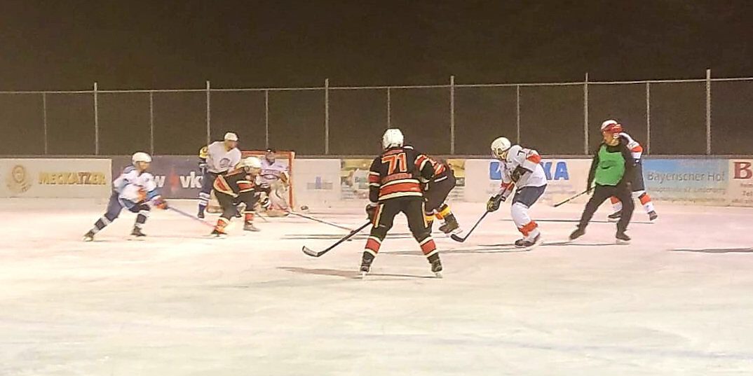 Eishockeyspiel auf dem Eisplatz Lindenberg, Teams in Schwarz und Weiß kämpfen um den Puck vor dem Tor.