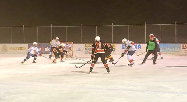 wp-16376066910971944333033173623629.jpg Eishockeyspiel auf dem Eisplatz Lindenberg, Teams in Schwarz und Weiß kämpfen um den Puck vor dem Tor.