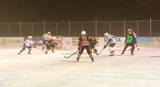 Eishockeyspieler im Wettkampf auf dem Eisplatz Lindenberg bei Nacht, umgeben von Werbebannern, intensives Spielgeschehen.