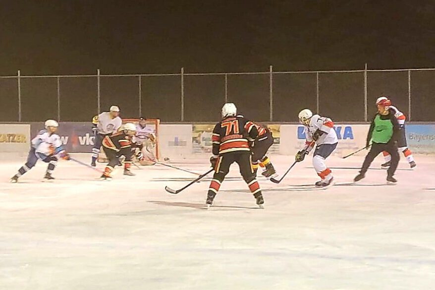 wp-16376066910971944333033173623629.jpg Eishockeyspiel auf dem Eisplatz Lindenberg, Teams in Schwarz und Weiß kämpfen um den Puck vor dem Tor.