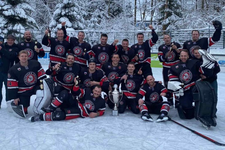 Aktuelles 1 Eine Eishockeymannschaft feiert auf dem Eis mit einem großen Pokal, umgeben von verschneiten Bäumen.