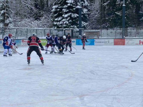 Eishockeyspiel auf einer eisigen Freiluftbahn, Spieler in actionreicher Szene, umgeben von schneebedeckten Bäumen.