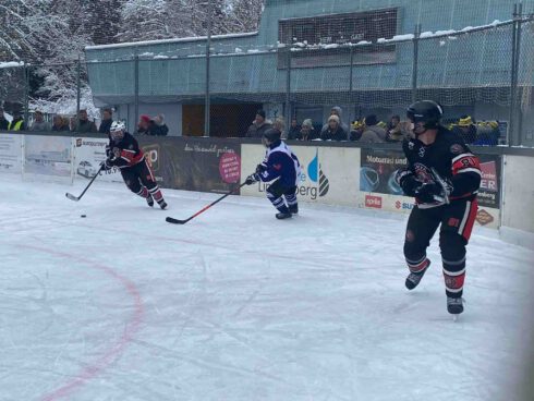 Beim Eishockeyspiel am Eisplatz Lindenberg verfolgen zwei Spieler in schwarzen Trikots den Puck vor Zuschauern.