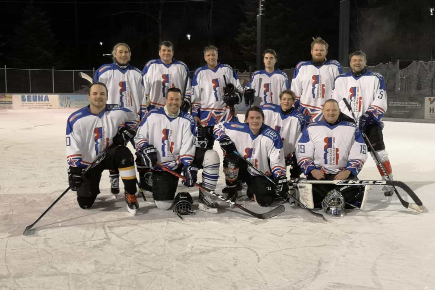 silverlines Eishockeymannschaft in weißen Trikots mit blau-roten Details posiert abends auf Eisfläche beim Eisplatz Lindenberg.