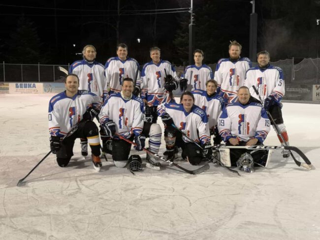 silverlines Eishockeymannschaft in weißen Trikots mit blau-roten Details posiert abends auf Eisfläche beim Eisplatz Lindenberg.