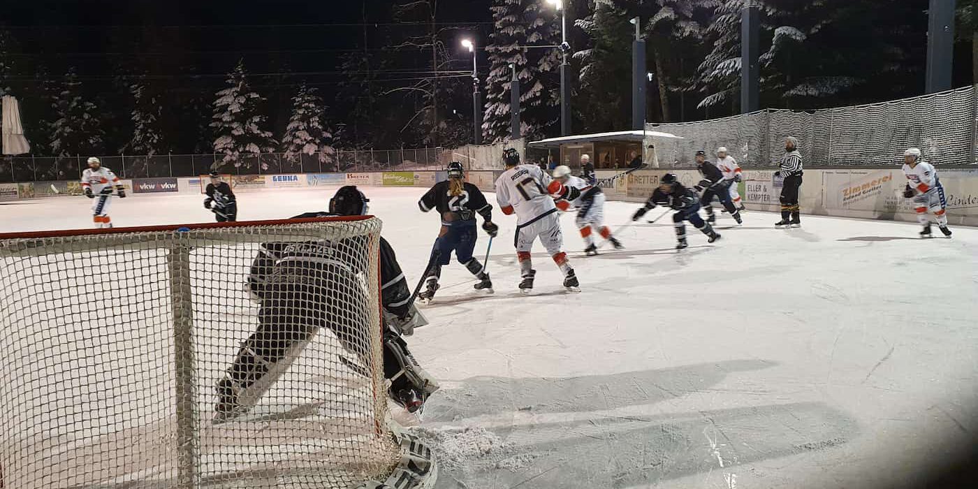 Eishockeyspiel bei Nacht auf dem Eisplatz Lindenberg, Spieler in Aktion vor dem Tor, winterliche Kulisse.