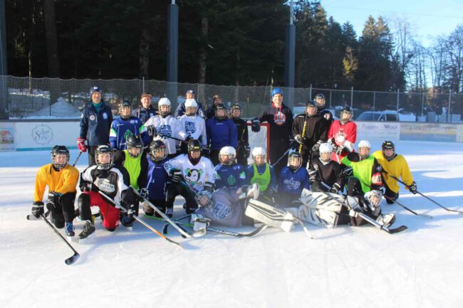 Eine Eishockeymannschaft in verschiedener Ausrüstung posiert lächelnd auf dem Eisplatz Lindenberg für ein Gruppenfoto.