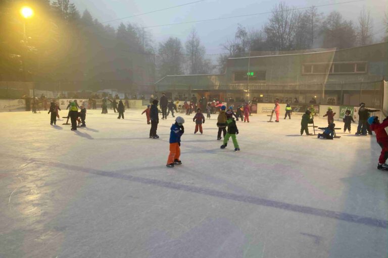 Publikumslauf Kinder und Erwachsene eislaufen auf dem Eisplatz Lindenberg an einem nebligen Tag, umgeben von Bäumen und Gebäuden.