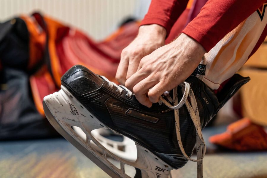 Person bindet Schlittschuhe auf einer Bank. Hände und Schlittschuhe im Fokus.