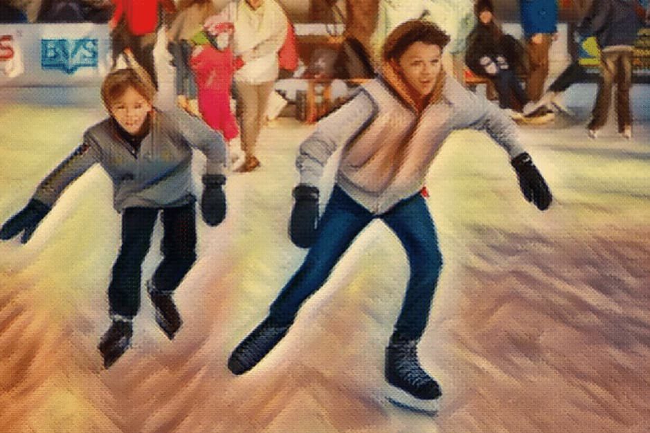 Zwei Kinder lernen im Kunsteisstadion Lindenberg Schlittschuhlaufen, umgeben von weiteren Eisläufern.