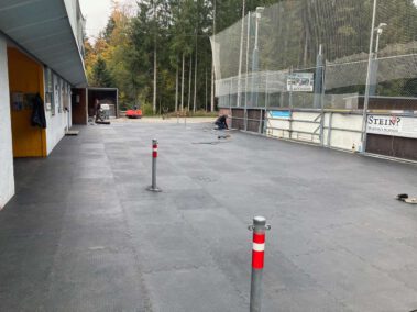 Nagelneue Matten am Vorplatz verlegt 3 Ein Mann arbeitet am Rand eines leeren Kunsteisstadions, das von Matten bedeckt ist, im Freien.