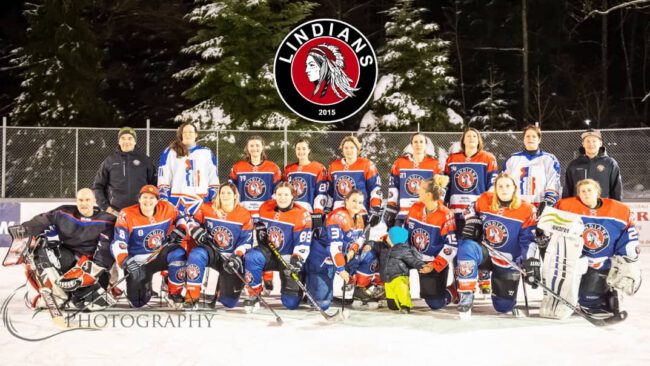 Lindians Damen-Eishockeymannschaft Eishockey-Team Lindians posiert in orangen Trikots auf Eisfläche unter dem Logo, umgeben von schneebedeckten Bäumen.