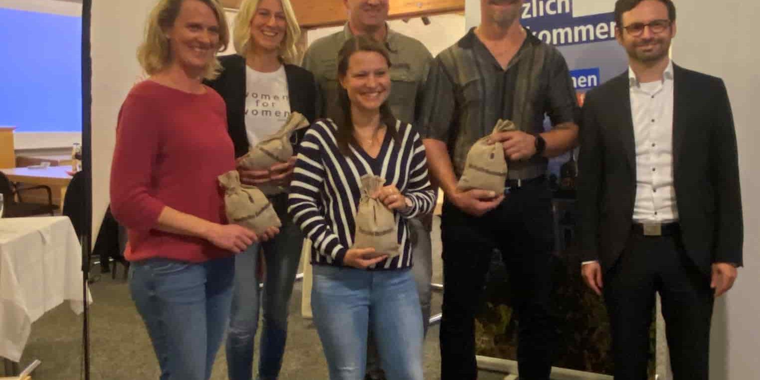 Sechs Personen posieren lächelnd mit Preisen vor einem Banner der Volksbank Lindenberg eG in einem Saal.