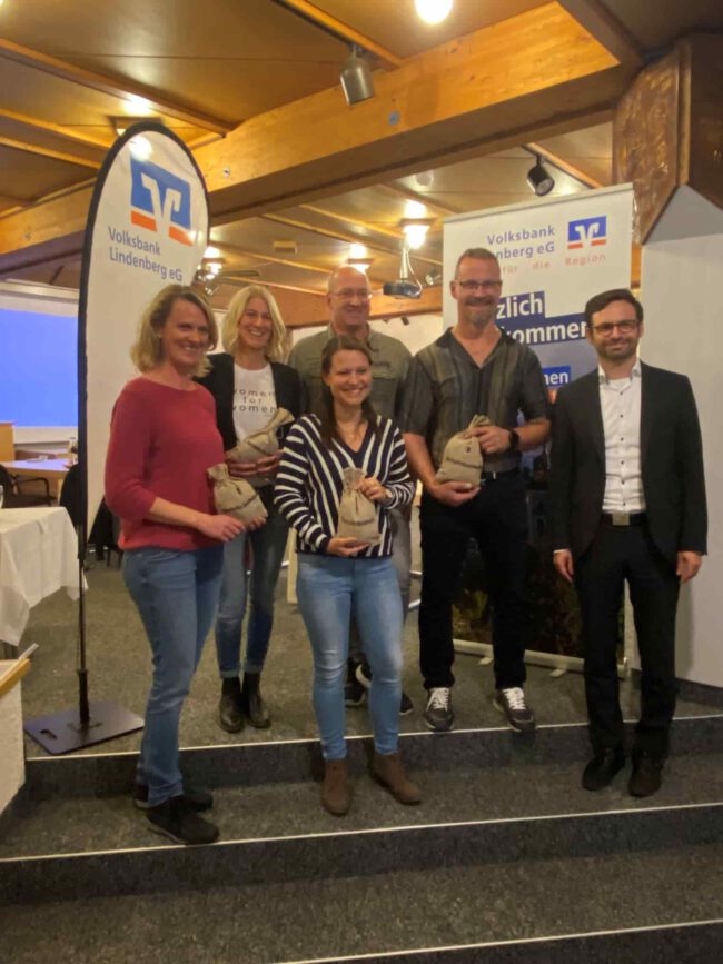 Volksbank-förderpreis Sechs Personen posieren lächelnd mit Preisen vor einem Banner der Volksbank Lindenberg eG in einem Saal.