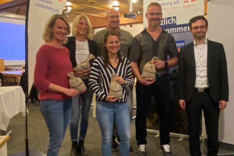 Volksbank-förderpreis Sechs Personen posieren lächelnd mit Preisen vor einem Banner der Volksbank Lindenberg eG in einem Saal.