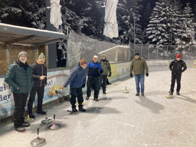 eisstockschiessen Menschen spielen Eisstockschießen auf dem Eisplatz Lindenberg, umgeben von schneebedeckten Bäumen in der Nacht.
