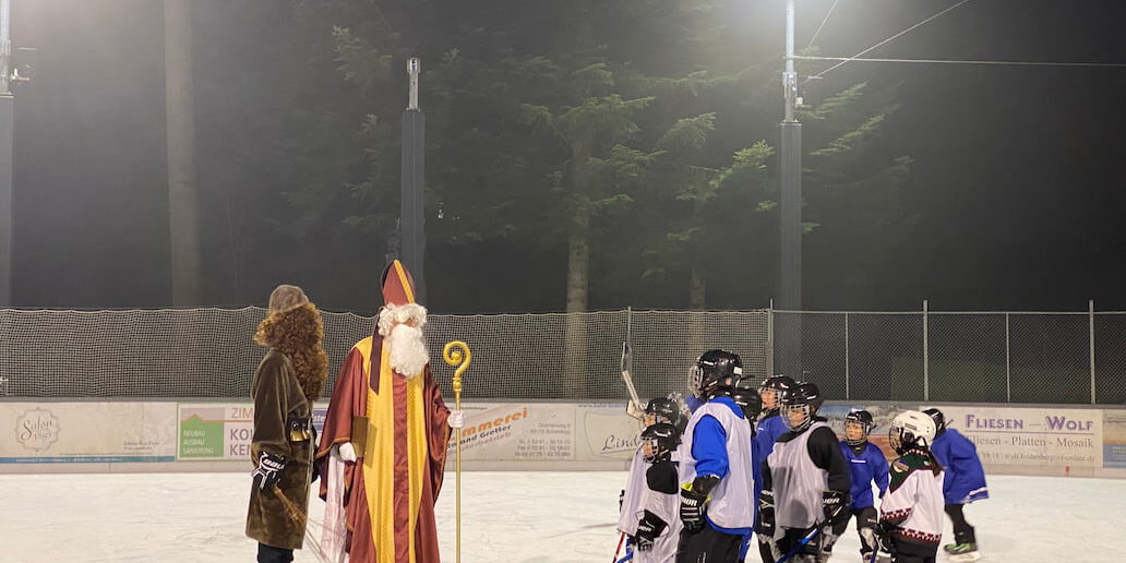 nikolaus am Eisplatz Lindenberg Nikolaus und Knecht Ruprecht begrüßen eine Gruppe von Kindern im Eishockey-Outfit auf einer mit Flutlicht beleuchteten Eisbahn.