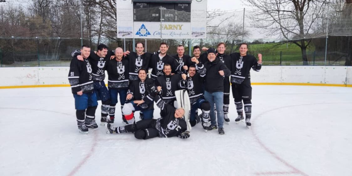Eishockeyteam Black Flyers auf dem Eisplatz Lindenberg, fröhlich posierend vor der Anzeigetafel im Freien.