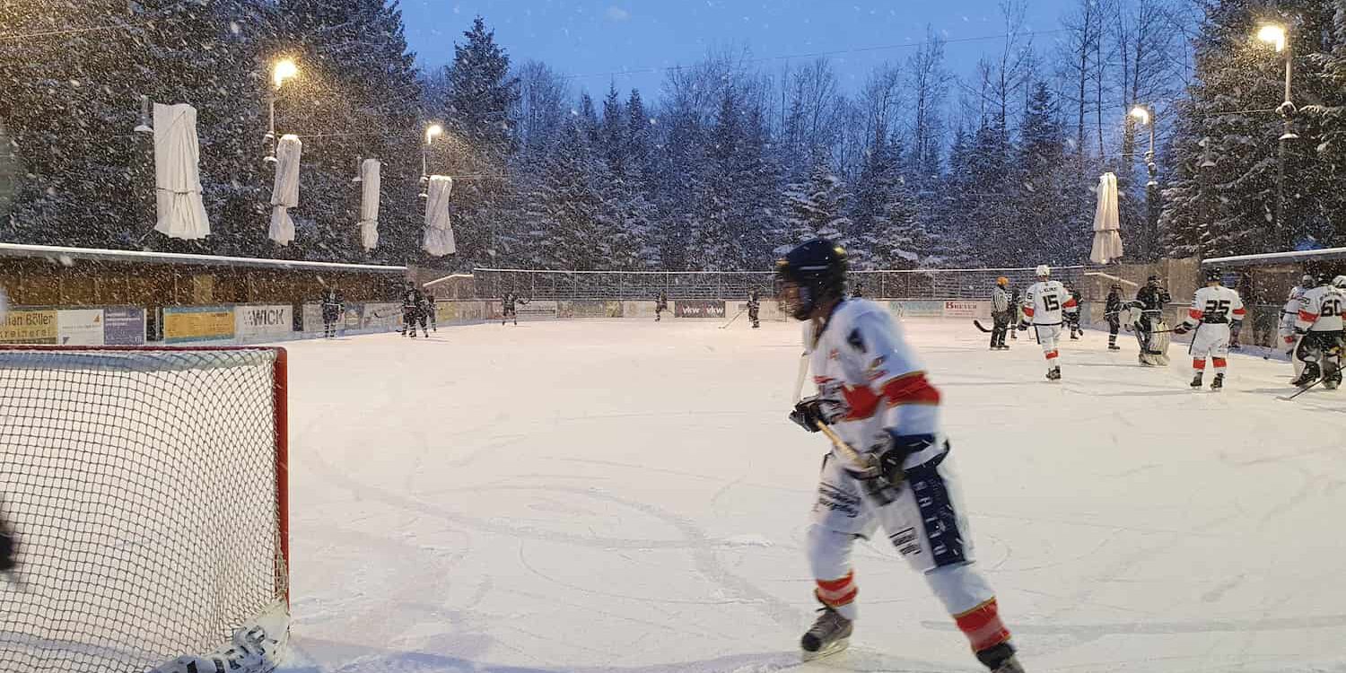 eiskratzer-eagles-21-01-23 Eishockey-Spieler auf dem verschneiten Eisplatz Lindenberg, die Eiskratzer Eagles im Einsatz, umgeben von winterlicher Kulisse.
