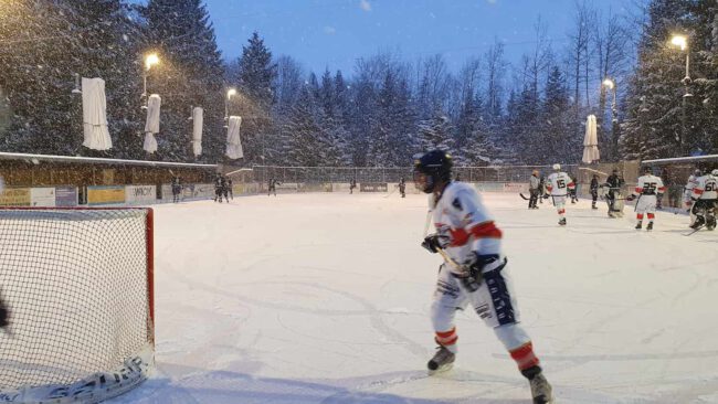 eiskratzer-eagles-21-01-23 Eishockey-Spieler auf dem verschneiten Eisplatz Lindenberg, die Eiskratzer Eagles im Einsatz, umgeben von winterlicher Kulisse.