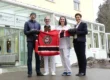 Vier Personen überreichen dem Krankenhaus Lindenberg ein rotes Hockeytrikot der Lindenberg Chiefs vor dem Gebäude.