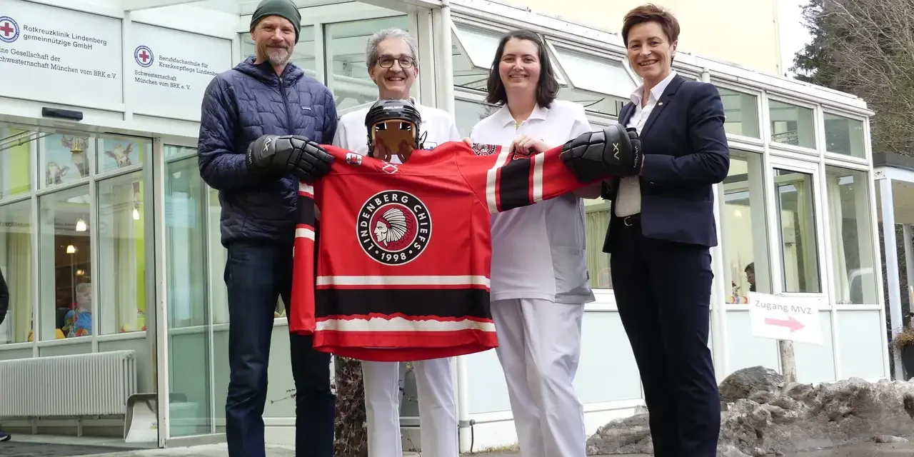 Vier Personen überreichen dem Krankenhaus Lindenberg ein rotes Hockeytrikot der Lindenberg Chiefs vor dem Gebäude.
