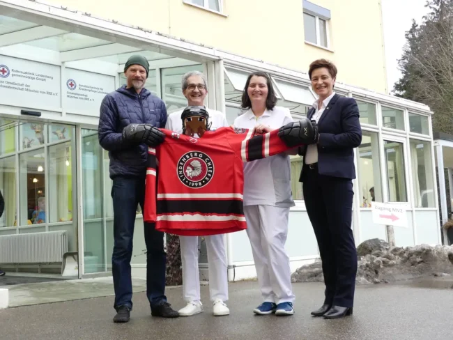 Vier Personen überreichen dem Krankenhaus Lindenberg ein rotes Hockeytrikot der Lindenberg Chiefs vor dem Gebäude.