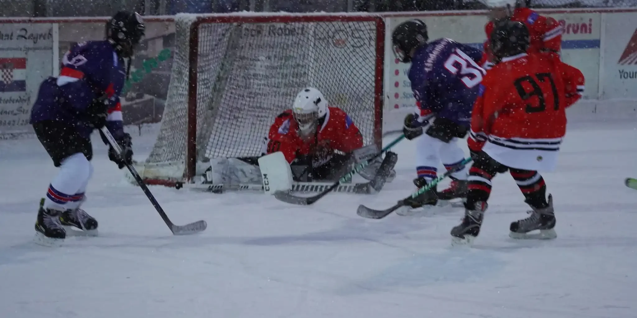 tvl-jugend-marktoberdorf-U15 Jugendeishockeyspiel beim TV Lindenberg, Torwart in Rot wehrt Puck ab, Spieler in Rot und Blau kämpfen am Tor.
