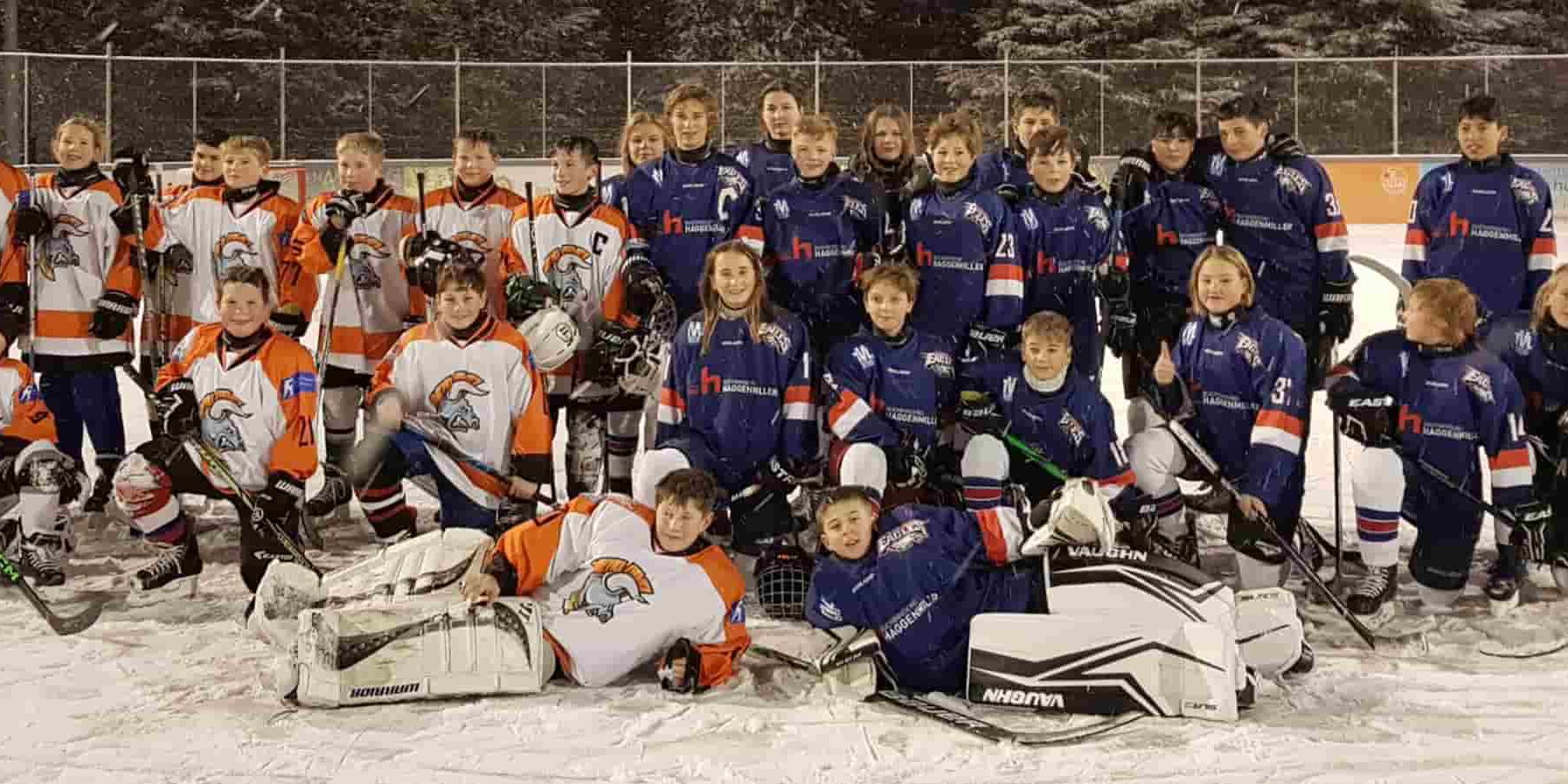 Eine Gruppe von jungen Eishockeyspielern in blauen und orangefarbenen Trikots posiert gemeinsam auf dem Eis.