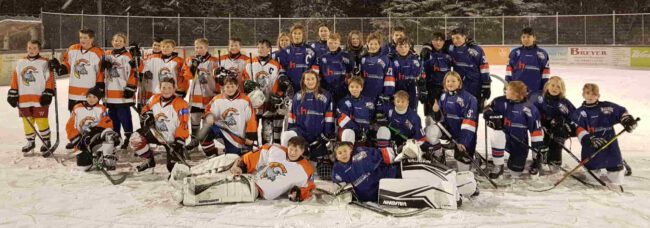 Eine Gruppe von jungen Eishockeyspielern in blauen und orangefarbenen Trikots posiert gemeinsam auf dem Eis.