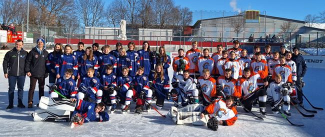 Jugend-Eishockeymannschaften posieren auf dem Eisplatz Lindenberg in bunter Ausrüstung bei sonnigem Winterwetter.