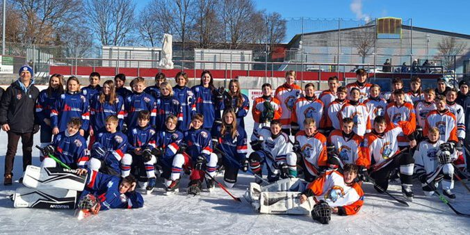 Jugend-Eishockeymannschaften posieren auf dem Eisplatz Lindenberg in bunter Ausrüstung bei sonnigem Winterwetter.