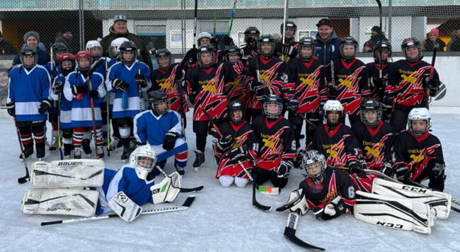 Bild1 Kinder-Eishockeyteams in blauen und schwarzen Trikots posieren gemeinsam auf dem Eisplatz von Lindenberg.