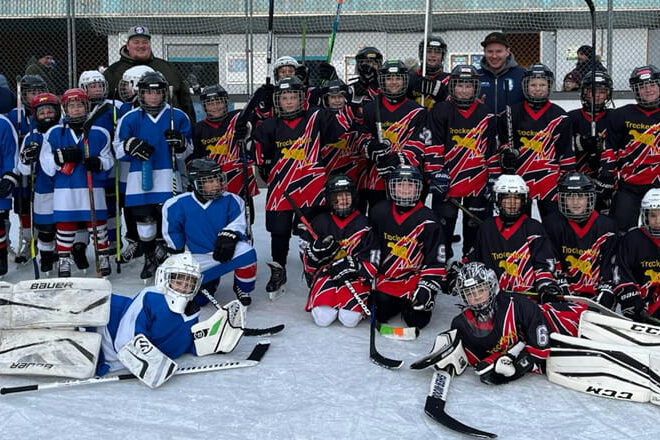 Bild1 Kinder-Eishockeyteams in blauen und schwarzen Trikots posieren gemeinsam auf dem Eisplatz von Lindenberg.