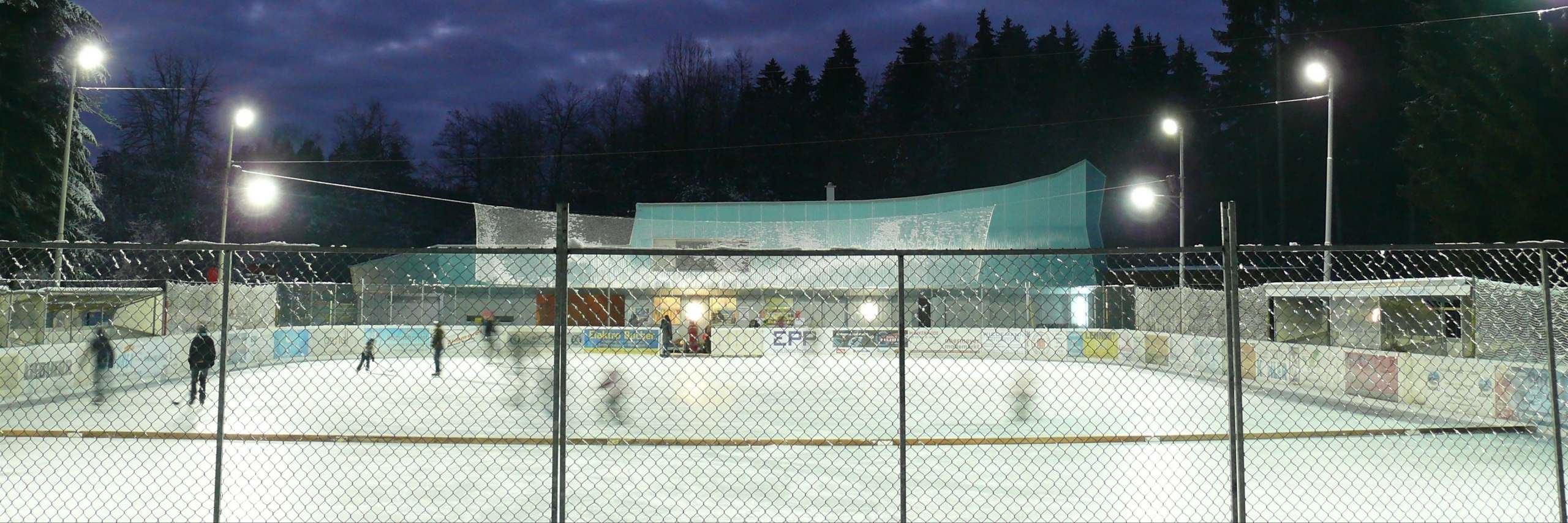 Eisplatz Lindenberg am Abend unter Flutlicht mit Eisläufern und Tribünengebäude