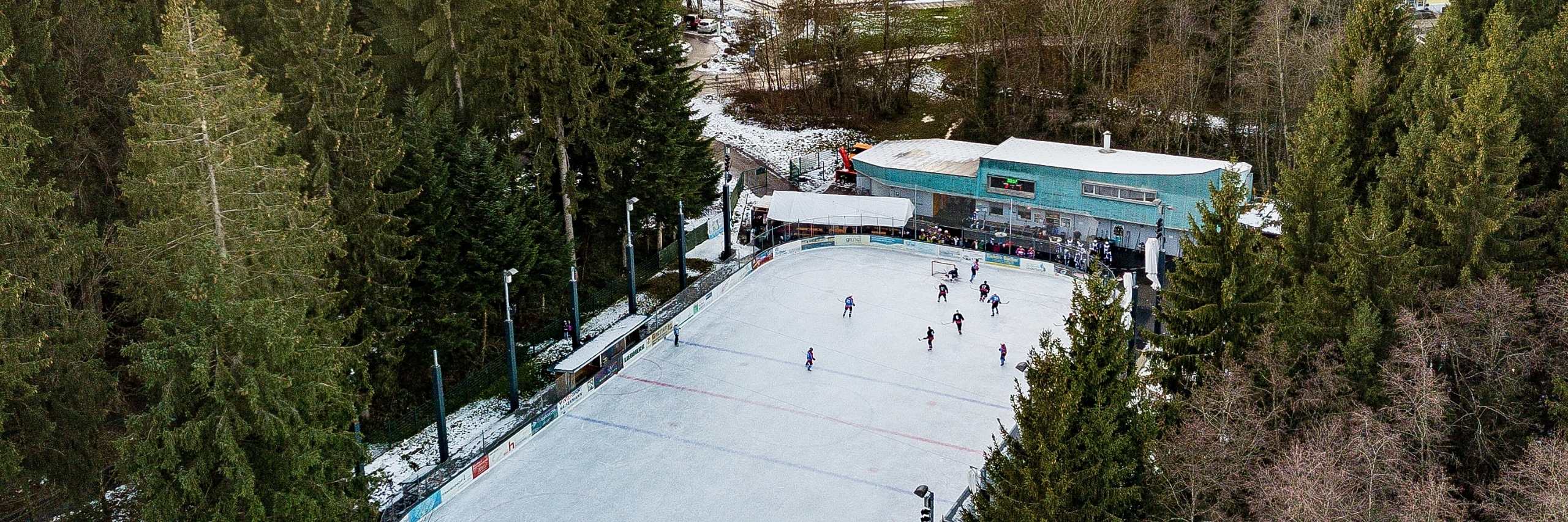 Luftaufnahme des Eisplatz Lindenberg im Wald mit Eisfläche und Tribünengebäude