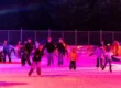 Kinder und Jugendliche laufen bei der Eisdisco im farbigen Scheinwerferlicht Schlittschuh auf dem Eisplatz Lindenberg.