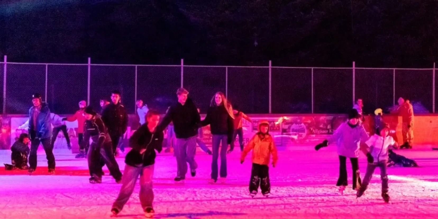 Kinder und Jugendliche laufen bei der Eisdisco im farbigen Scheinwerferlicht Schlittschuh auf dem Eisplatz Lindenberg.