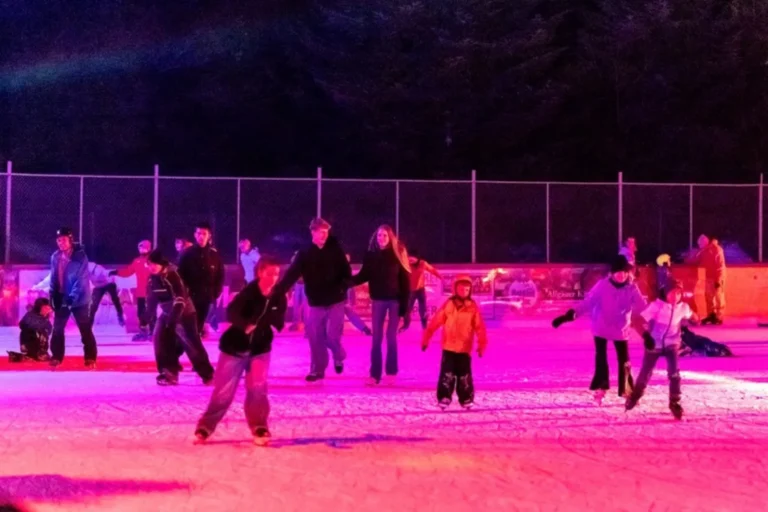 Kinder und Jugendliche laufen bei der Eisdisco im farbigen Scheinwerferlicht Schlittschuh auf dem Eisplatz Lindenberg.