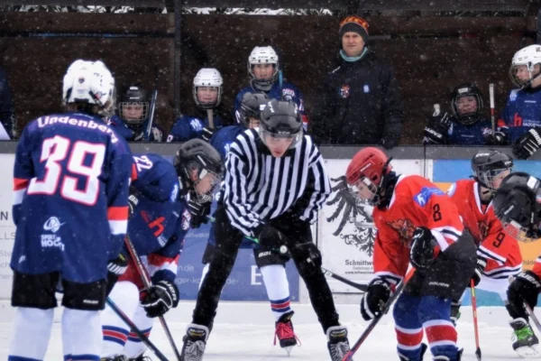 Bully beim Nachwuchs-Eishockey in Lindenberg: Schiedsrichter zwischen Spielern in blauen und roten Trikots, Schneefall.